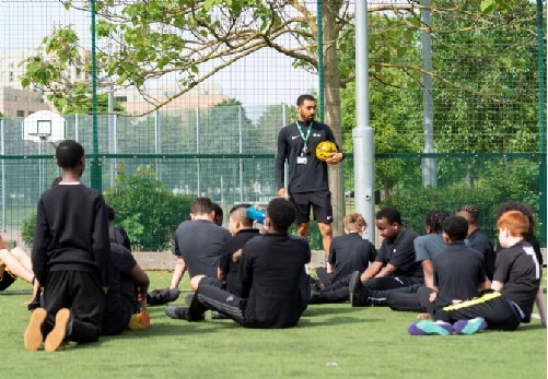 Students listen to their PE teacher Mr Walker on the MUGA talking to students at football